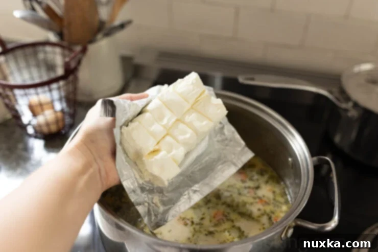 Cubed cream cheese melting into a pot of chicken chowder, creating a rich, creamy texture.
