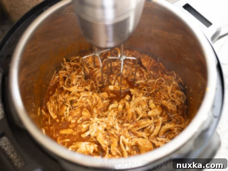 Image of shredding the Instant Pot chicken enchiladas with a hand mixer